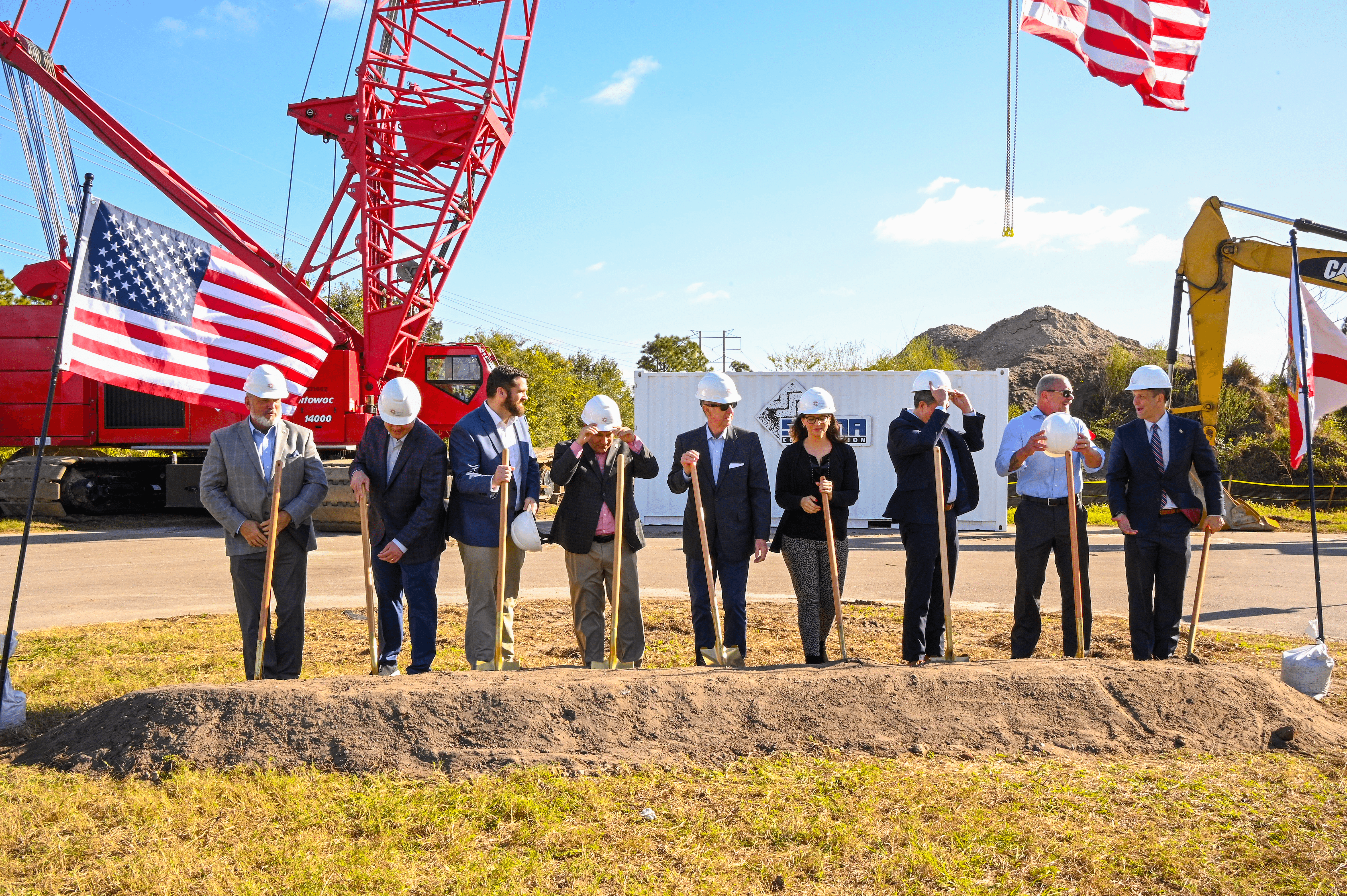 A group of 9 people in hardhats initiating the groundbreaking in front of a crane