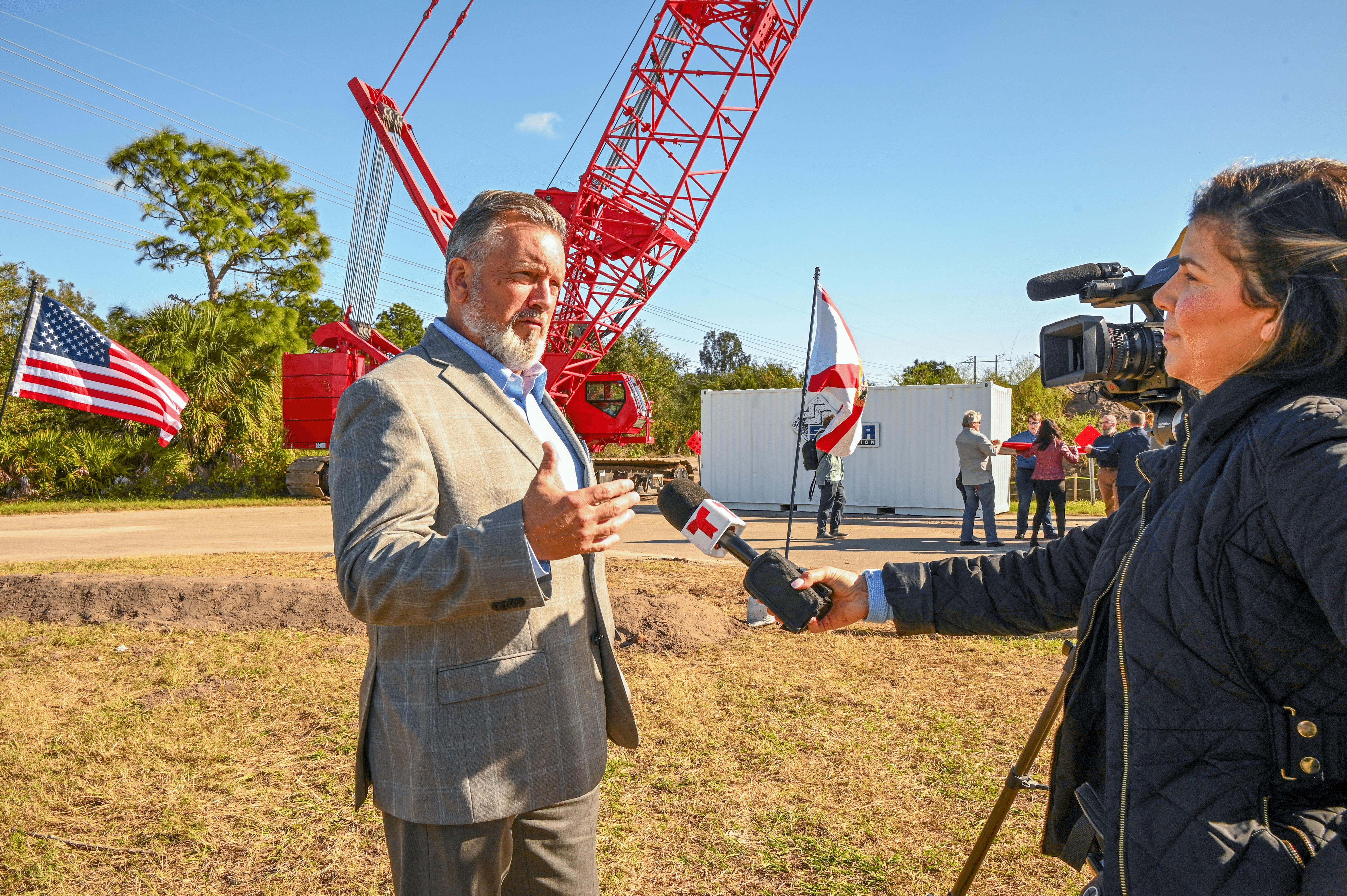 A man answering questions about the groundbreaking. A red crane is shown in the background.